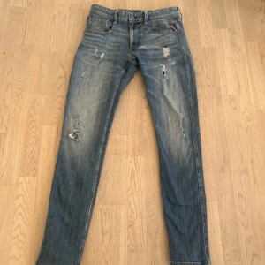 Replay anbass - Säljer ett par replay jeans, size 31/34 i blå tvätt med slitningar och hål för en riktigt avslappnad vibe. Jeansen har smal passform och klassisk femficksdesign. Perfekta för dig som gillar en streetig look.