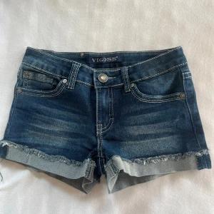 Jeansshorts - Mörkblå jeansshorts från Vigoss med snygga slitningar och fransig kant nertill. Baksidan har stora broderade fjärilar med silverdetaljer