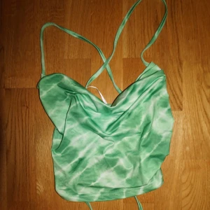 Grön tie-dye linnetopp med snörning - Säljer en grön och vit tie-dye linnetopp med tunna axelband och snygg snörning i ryggen. Toppen har en draperad framsida och croppad passform, perfekt för att sticka ut med en cool och trendig look.