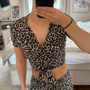 Leopardmönstrad knytblus från Vero Moda - Säljer en kortärmad blus från Vero Moda med leopardmönster i svart och beige. Toppen har v-ringning, knappar framtill och en snygg knytning i midjan. Passar perfekt till leopardkjolen som jag också säljer 🐆💗