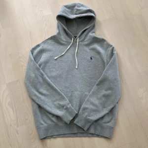 Ralph Lauren hoodie - Säljer en klassisk, stilren grå hoodie från Polo Ralph Lauren med broderad marinblå logga på bröstet. Tröjan är casual och passar till allt! Skick är 10/10, inte använd mycket. 
