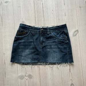 Blå lågmidjad jeanskjol  - Mörkblå fransad lågmidjad jeanskjol från Yessica i fint skick. Kan inte hitta storlek men skulle säga S/M. Tvärs över midjan är det 40 cm och den är ca 32-33 cm lång. Använd gärna köp nu!