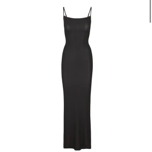 Svart lång slipklänning från Skims - Supersnygg svart lång slipklänning från Skims med smala axelband och figurnära passform. Klänningen har en minimalistisk look och är tillverkad i ett mjukt, stretchigt material som sitter perfekt på kroppen. Endast använd en gång och köpt för mindre än en månad sen! 