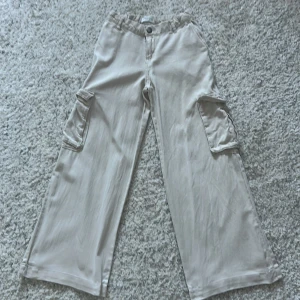 Beiga cargobyxor wide från Lindex - Snygga beiga cargobyxor från Lindex i storlek 146. Byxorna har breda ben, fickor på sidorna och resår i midjan. Perfekta för en avslappnad och trendig look. Använt fåtal gånger.