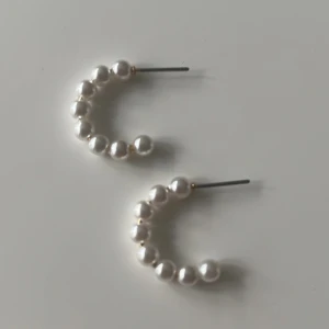 Pärlörhängen i halvmåneform - Snygga örhängen i halvmåneform med vita pärlor på rad. Perfekta för dig som vill ha en klassisk men ändå trendig look. Metallstift i silverfärg och små gulddetaljer mellan pärlorna. Lätta att matcha med olika outfits. Köpta på glitter