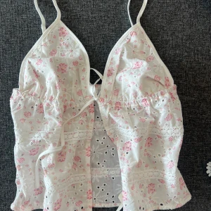 Vit blommig linnetopp med spets - Supersöt vit linnetopp med rosa blommor, broderade detaljer och spetsinslag. 