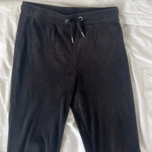 Svarta mjukisbyxor från Gina Tricot - Svarta mjukisbyxor från Gina Tricot med bootcut-ben och snörning i midjan. Byxorna har två bakfickor och är gjorda i ett mjukt material som känns skönt mot huden. Perfekta för chill dagar eller när du vill vara extra bekväm.