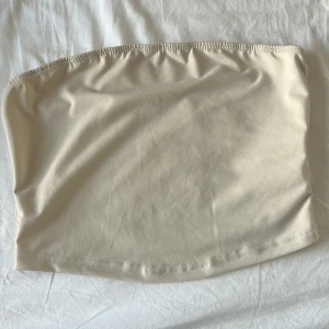 Beige tubtopp - Enkel och stilren beige tubtopp från SHEIN. Toppen är axelbandslös och har en mjuk, stretchig känsla som sitter skönt mot kroppen. Perfekt att styla med jeans eller kjol för en clean look. OBS, katt finns i hemmet!