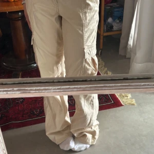Beige cargopants med fickor - Säljer ett par beige cargopants med stora sidofickor och avslappnad passform. Byxorna har resår i midjan och är gjorda i jeans liknande material. Varan är ifrån Gina Young och är i storlek 158 fast de passar mig som är en xs och ca 158 cm lång