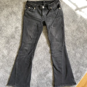 True Religion Joey Low Rise Flare Jeans - Snygga gråa jeans från True Religion, modell Joey Low Rise Flare. De har låg midja och utsvängda ben, klassiska bakfickor med logga och silverfärgade knappar. Perfekta för dig som gillar en retro vibe och vill sticka ut med en cool siluett. Använda ca 4-5 gånger på grund av viktnedgång så dom blev förstora för mig tyvärr och kan inte ha dom. Hittade inte lappen till dom men dom är helt ny skick med inga tecken på skada.
