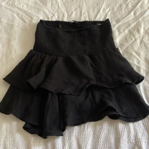 Svart volangkjol från SHEIN XS - Supersöt svart kortkjol från SHEIN i storlek XS. Kjolen har bred smock i midjan och flera lager volanger som ger en flowy och trendig look. Perfekt att styla med crop top eller stickad tröja för en cool vibe.