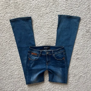 Blå lågmidjade bootcut jeans - Snygga blå jeans från Mywear i bootcut-modell med klassiska fem fickor, slitningar och bruna läder detaljer! Innerbenslängd: 81 cm. Midjeberedd: 32 cm. Benbredd: 21 cm❤️