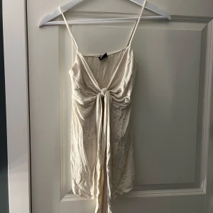 Krämvit topp med knyt - Söt krämvit topp med smala axelband och snygg knytning framtill. Toppen har en figurnära passform och är perfekt för varma sommardagar. Enkel och stilren design som passar dig som gillar minimalistiskt mode.