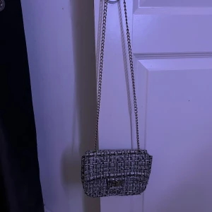 Svartvit axelväska med kedja🤍 - Snygg axelväska i svartvitt rutigt tyg med silverfärgad kedjerem. Väskan har ett klassiskt lock med vridlås och är perfekt för att bära det viktigaste. Stilren och trendig modell som passar till många outfits.🤍🤍
