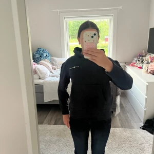 Mörkblå hoodie från Sail Racing - Mörkblå hoodie från Sail Racing med vit logga på bröstet och stor känguruficka framtill. Tröjan har huva med tryck på. Den är i strl 160.