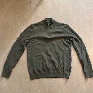 Olivgrön half zip-tröja Bondelid S - Olivgrön långärmad tröja från Bondelid med ribbad krage och half zip-dragkedja. Tröjan är i mjuk bomull och har en klassisk, normal passform. Diskret logga