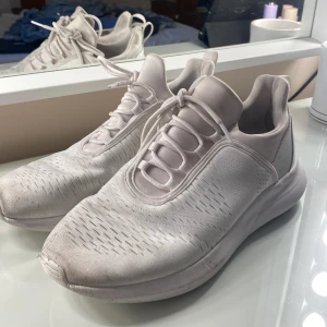 Vita sneakers med snörning - Snygga vita sneakers med modern design och rund tå. Ovandelen är i textil med diskreta mönsterdetaljer och snörning framtill. Skorna har en platt sula och är perfekta för en clean och sportig look.