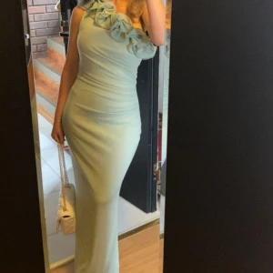 Ljusgrön långklänning med volang - Supersnygg ljusgrön långklänning med figurnära passform och stora volangdetaljer vid axeln. Klänningen är ärmlös och har en elegant, stilren look som verkligen sticker ut. Perfekt för dig som vill ha något unikt och trendigt.