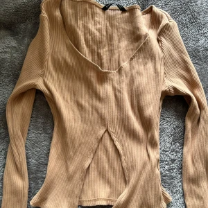 Beige ribbad långärmad topp SHEIN - Trendig beige ribbad topp från SHEIN med lång ärm och v-ringad hals. Snygg detalj med slits framtill som ger en cool twist. Perfekt att styla med jeans eller kjol för en chill look.