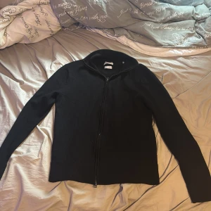 Svart merinoullskofta från These Glory Days - Svart kofta i mjuk och lyxig merinoull från These Glory Days. Modellen har hel dragkedja framtill, hög krage och långa ärmar. Perfekt för lager-på-lager och stilren look. Snygg och enkel att matcha med det mesta. Nypris 1099kr kom med frågar och prisförslag