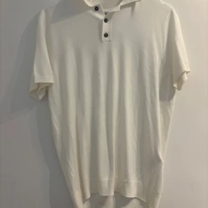 Vit pikétröja från Zara i bomull - Klassisk vit pikétröja från Zara i storlek M. Tröjan har korta ärmar, tre knappar framtill och är tillverkad i mjuk bomull. Aldrig använd 