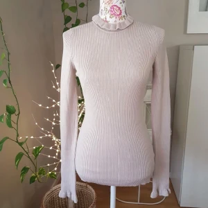 Beige ribbad tröja med volangkrage - Supersöt ribbad beige tröja från Gina Tricot med långa ärmar och volangdetaljer vid hals och ärmslut. Tröjan är figurnära och har en mjuk, stretchig känsla. Perfekt för dig som gillar en feminin och stilren look!💞