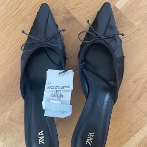Svarta spetsiga klackar från Zara - Svarta pumps från Zara med spetsig tå, låg klack och dekorativ rosett framtill. Skorna är tillverkade i ett slätt, satinliknande material och har en elegant siluett. Helt oanvända, storlek 38, nypris 499. 