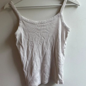Vit ribbad linnetopp - Enkel och stilren vit ribbad linnetopp med smala axelband. Perfekt att matcha med jeans eller kjol för en clean look. Tunt och mjukt material som känns skönt mot huden.