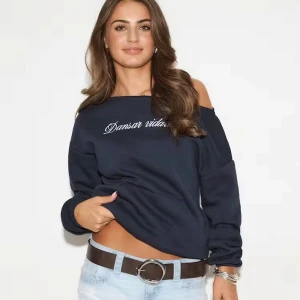 Mörkblå offshoulder sweatshirt - Mörkblå tröja med offshoulder och vit ”Dansar vidare i livet”  text framtill. Tröjan har lång ärm och en lös passform. Den är superfin men kommer inte till användning längre 🤍 