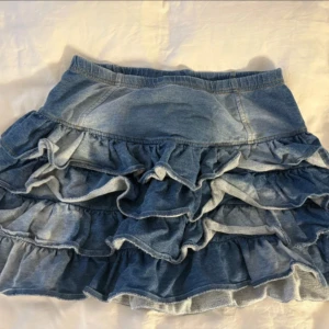 Volangkjol i jeans - Supersöt kort jeanskjol med flera volanger och bred resår i midjan. Kjolen är i klassisk blå denim och har en lekfull, rufsig look som ger extra volym❤️