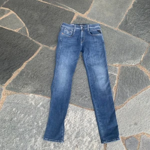 Blå Replay jeans slim fit 28/32 - Snygga blå jeans från Replay i modellen slim fit med klassisk femficksdesign och diskreta slitningar. Jeansen har raka ben, normal midja och är tillverkade i mjukt denimtyg. Perfekta för dig som gillar en stilren och tidlös look.