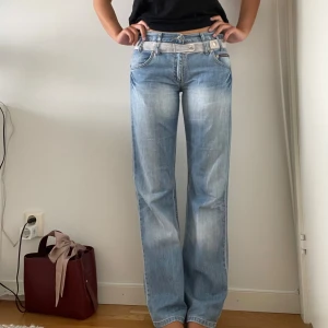 Ljusblåa jeans från Decant - Snygga ljusblå jeans från Decant med raka ben och coola slitningar. Byxorna har en unik detalj med breda bälteshällor och kontrasterande band i midjan. Jag är 172cm