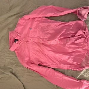 Rosa skjorta från Polo Ralph Lauren S - Snygg rosa skjorta från Polo Ralph Lauren i slim fit-modell. Skjortan har långa ärmar, klassisk krage och knäppning framtill. Detalj med blå broderad logga på bröstet och rutigt tyg på insidan av kragen. Perfekt för dig som vill sticka ut med färg.