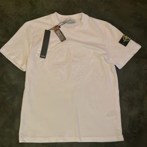 Vit Stone Island t-shirt med logga - Vit t-shirt sprillans ny från Stone Island med stor, upphöjd logga på bröstet och klassisk patch på ärmen. Skön passform och tillverkad i 100% bomull. Perfekt för dig som gillar stilrena och exklusiva plagg med streetkänsla. Pris kan diskuteras 