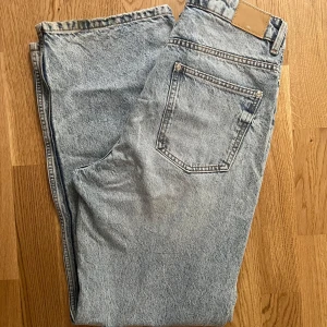 Ljusblå jeans från Zara, storlek 40 - Säljer ett par ljusblå jeans från Zara i klassisk femficksmodell. Jeansen har en snygg tvättad look, raka ben och normal passform. Tillverkade i bomull med detaljer i silverfärgad metall och brunt läderpatch bak i midjan.