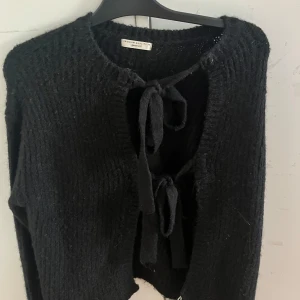 Svart stickad kofta  - Mysig svart stickad kofta från Gina Tricot med två knytband framtill. Koftan har långärmad design och en lite fluffig, grovstickad struktur som ger en trendig look. Perfekt att slänga över en topp för extra värme och stil. Storlek XS och är helt ny i skicket, aldrig använd 🤍🤍