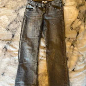 Gråa utsvängda jeans från Gina Tricot, strl 152 - Snygga grå jeans från Gina Tricot i storlek 152. Jeansen har klassisk femficksdesign, utsvängda ben och knäppning med tre knappar framtill. Perfekta till en avslappnad stil och funkar året runt.