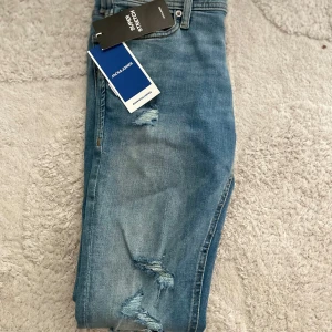 Skinny jeans från Jack & Jones - Snygga ljusblå skinny jeans från Jack & Jones med superstretch och slitna detaljer på benen. Klassisk femficksmodell med normal midja och bekväm passform. Perfekta för dig som gillar en modern och avslappnad stil.