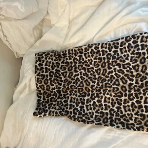 Leopardmönstrad kjol från Lindex  - Snygg leopardmönstrad kjol från lindex i stretchigt material. Kjolen har en rak passform och är i bruna, svarta och beige toner. Perfekt för dig som vill sticka ut med ett djurmönster och skapa en cool look.