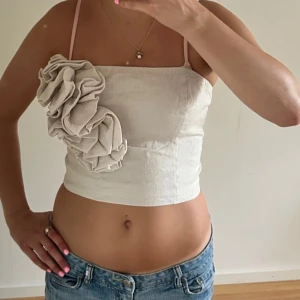 Beige tubb top med blomma  - Supersnygg tubb top i  beige en blomma. Toppen är figurnära och har smock baktill för extra komfort. Perfekt för dig som vill sticka ut med en unik och trendig look.