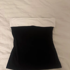 Svart och vit tubtopp från  - Säljer en stilren svart tubtopp från SHEIN med en bred vit kant upptill. Toppen är axelbandslös och har en klassisk bandeau-form som sitter tight mot kroppen. Materialet är  lite fleece aktigt och den är aldrig använd 💕