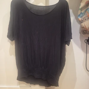 Svart loose topp med ribbad kant - En svart, lös topp med rund halsringning och korta ärmar. Toppen har en bred, ribbad kant nedtill som ger en avslappnad och cool siluett. Perfekt för dig som gillar en enkel men ändå snygg stil.