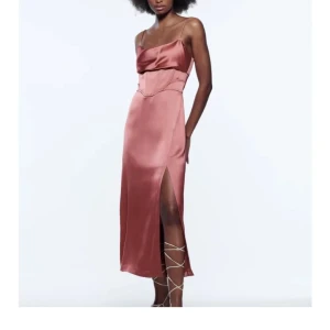 Rosa satinklänning med slits - Säljer en lång, glansig rosa klänning i satin med smala axelband och snygg slits framtill. Klänningen har en draperad byst och markerad midja som ger en elegant siluett.    Helt ny och oanvänd! Inköpt för 559kr. Egen bild, men dåligt ljus, ser mer ut som på bilderna från hemsidan. 