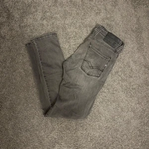 Replay Anbass grå jeans slim fit 30/32 - Säljer ett par grå Replay Anbass jeans i slim fit med klassisk femficksdesign och snygga detaljer på bakfickorna. Jeansen har en smal passform och är tillverkade i mjukt bomullsmaterial med lite stretch för extra komfort.