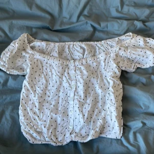 Vit offshoulder blus med prickar från HM - Charmig vit offshoulder blus med små svarta prickar och korta puffärmar. Perfekt för en somrig look med elastiska kanter för en bekväm passform.