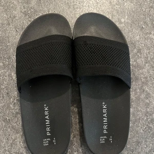 Svarta sandaler från Primark stl 39 - Svarta sandaler från Primark i storlek 39. De har en bred, stickad rem över foten och en platt sula i syntetmaterial. Perfekta för sommardagar och riktigt sköna att glida i. Enkel och stilren design som passar till det mesta. Endast använda inomhus, som ni ser på bilderna är det lite skavanker samt lite fläckar. 