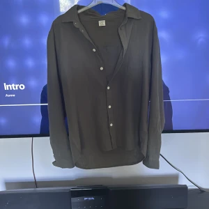 Olivgrön skjorta  - Säljer en olivgrön skjorta från Lindex i storlek 170. Skjortan har långa ärmar, klassisk krage och knäppning framtill med vita knappar. Perfekt för en stilren och avslappnad look. Passar xs-S