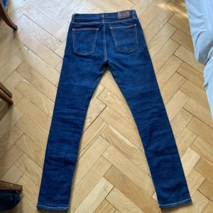 Nudie Jeans Mörkblå - Säljer ett par mörkblå jeans från Nudie Jeans i storlek 30/32 med klassisk femficksdesign och kontrastsömmar. Jeansen har en slim passform och är tillverkade i slitstarkt denimtyg. Perfekta för dig som gillar stilrena och tidlösa jeans. Såklart äkta ✅Nypris 1900 💸Skriv vid fråga