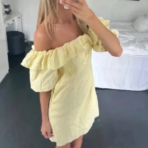 Gul offshoulder klänning med volang - Söt gul klänning med offshoulder-design och stora volangdetaljer upptill. Klänningen är kort och har en luftig passform, perfekt för varma dagar. 