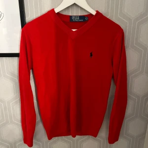 V-ringad tröja från Ralph Lauren - Klassisk röd v-ringad tröja från Polo Ralph Lauren med broderad logga på bröstet. Långärmad modell i mjukt material, perfekt för lager-på-lager och stilrena outfits. Storlek M men passar S.